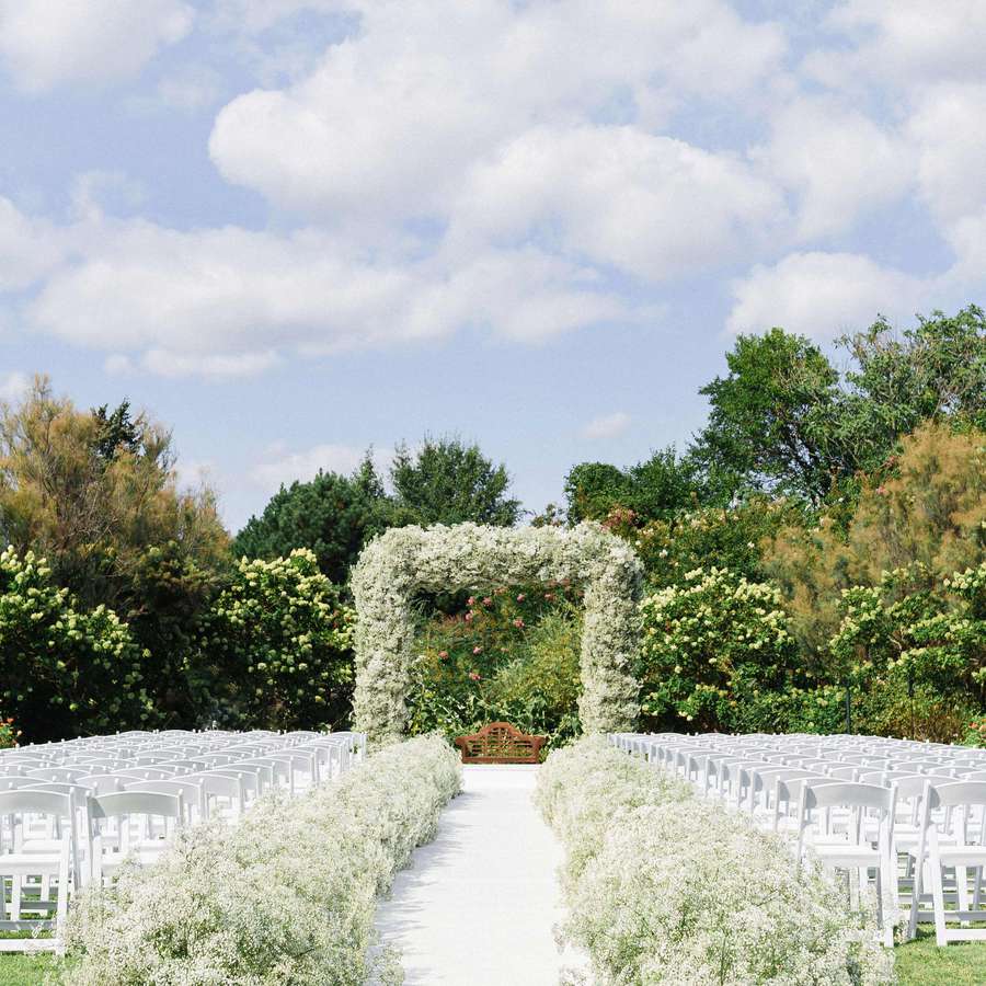 Wedding ceremony setup with arch and aisles lined with baby's breath