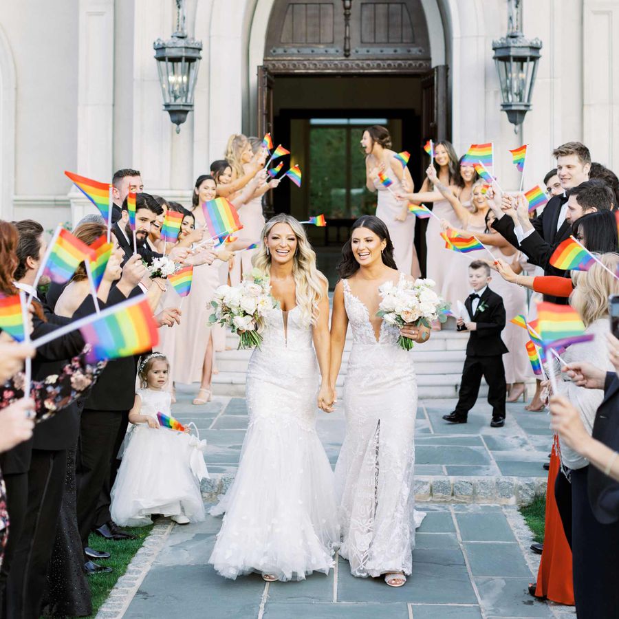 Brides walk holding hands surrounded by rainbow pride flags