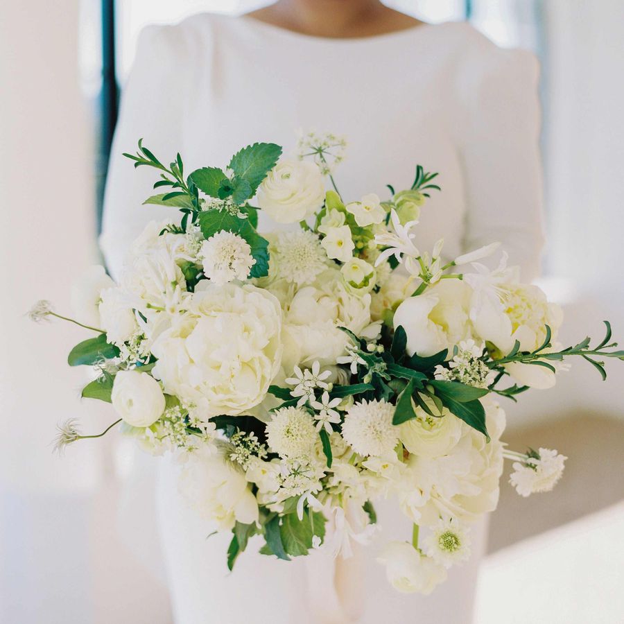 Bride carrying white bouquet with garden roses, ranunculus, sweet peas, hellebores, and peonies
