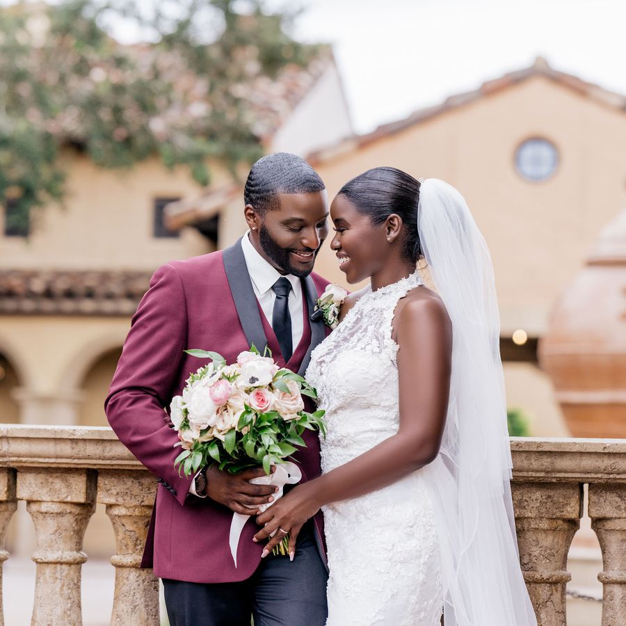 Groom in a burgundy tux and bride in a high-neck floral dress 