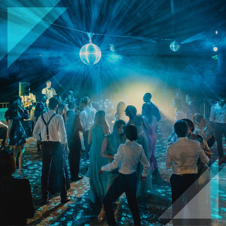 Wedding guests dance on a blue-lit dance floor below a disco ball.