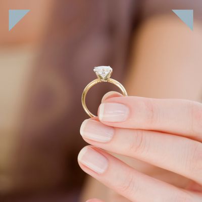 hands with manicured nails holding yellow gold solitaire engagement ring