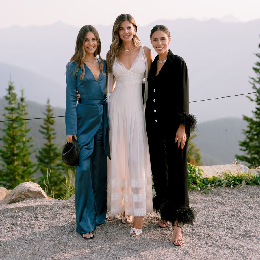 bride wearing a white lace dress, in between two bridesmaids wearing chic two-piece rehearsal dinner looks