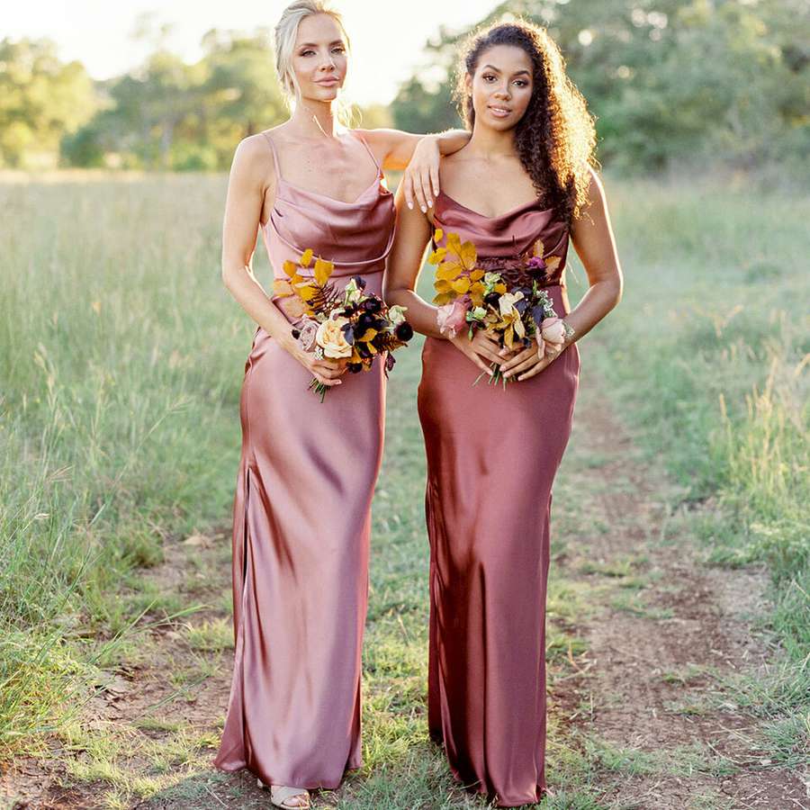 Two bridesmaids wearing Revelry Skye Satin dresses while standing in a field