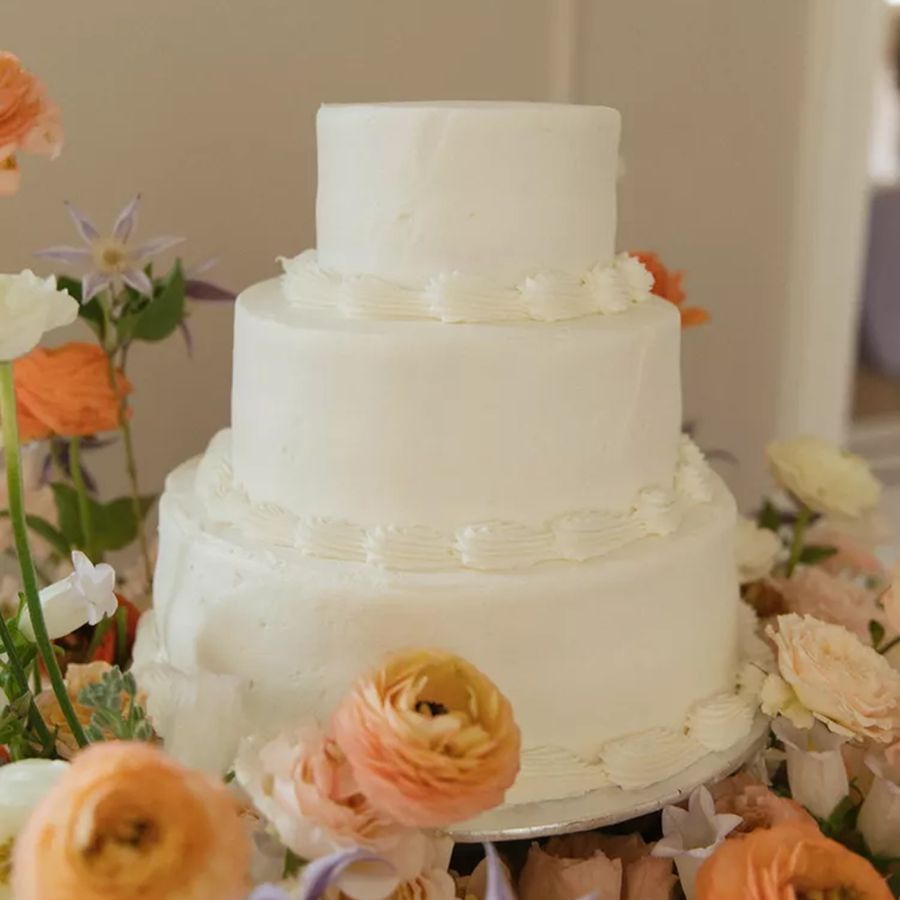 Three-Tiered White Sam's Club Wedding Cake with Decorative Buttercream Frosting Surrounded by Fresh Flowers