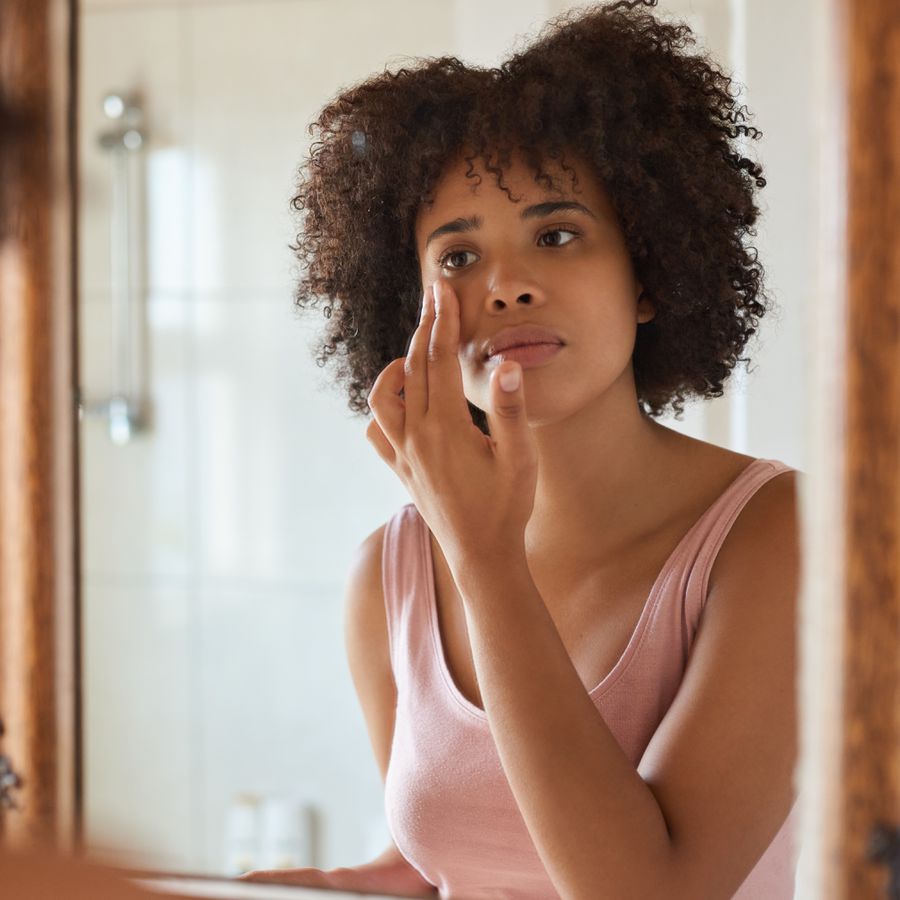 A woman putting moisturizer on her face while looking at herself in the mirror