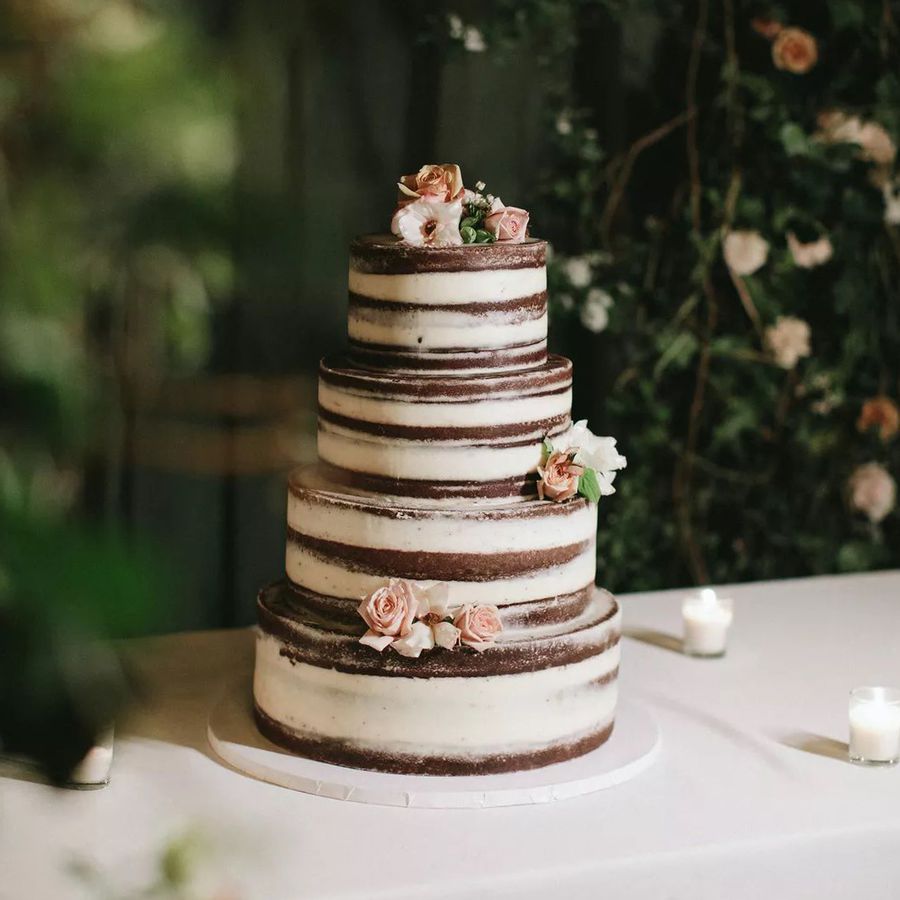 Naked chocolate wedding cake with pink roses and white florals on white table