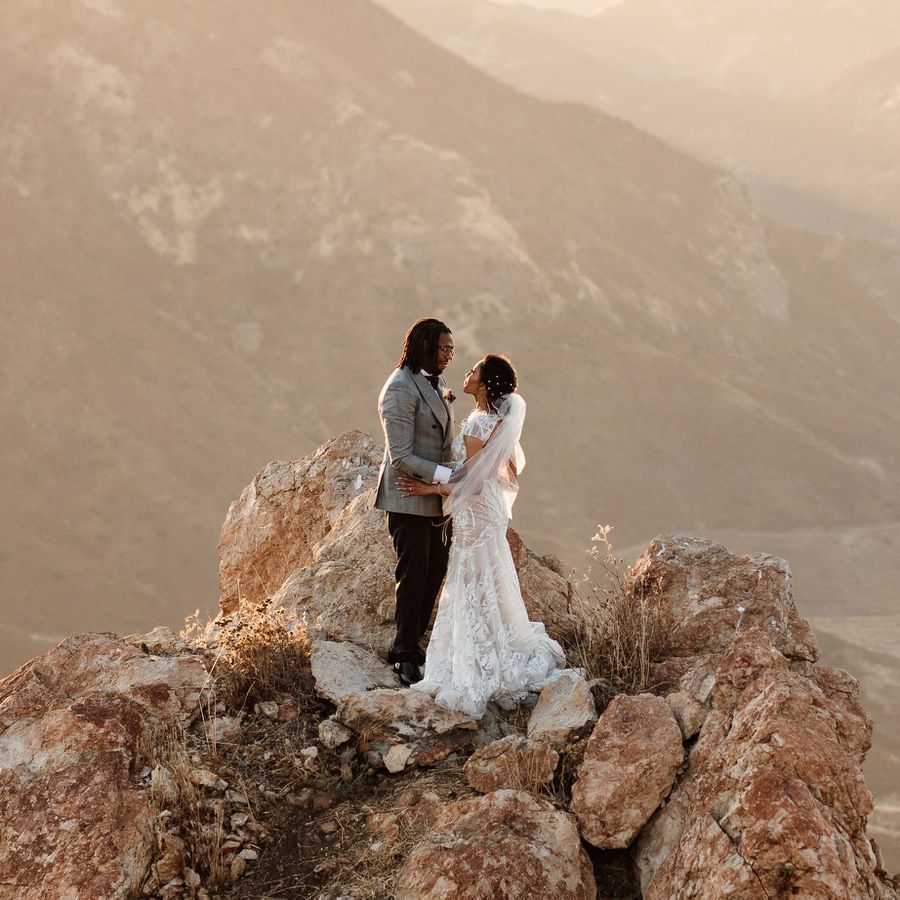 A bride and groom embracing on top of a mountain, happily married.