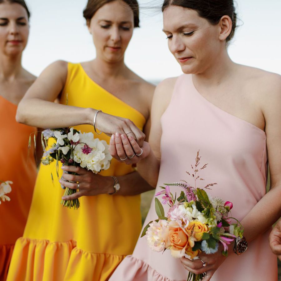 Bridesmaids in colorful one-shoulder dresses holding bouquets and passing rings