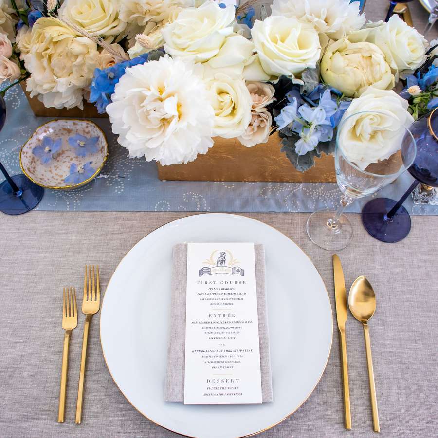 Place setting at a wedding tablescape with a white, cream, and blue floral centerpiece