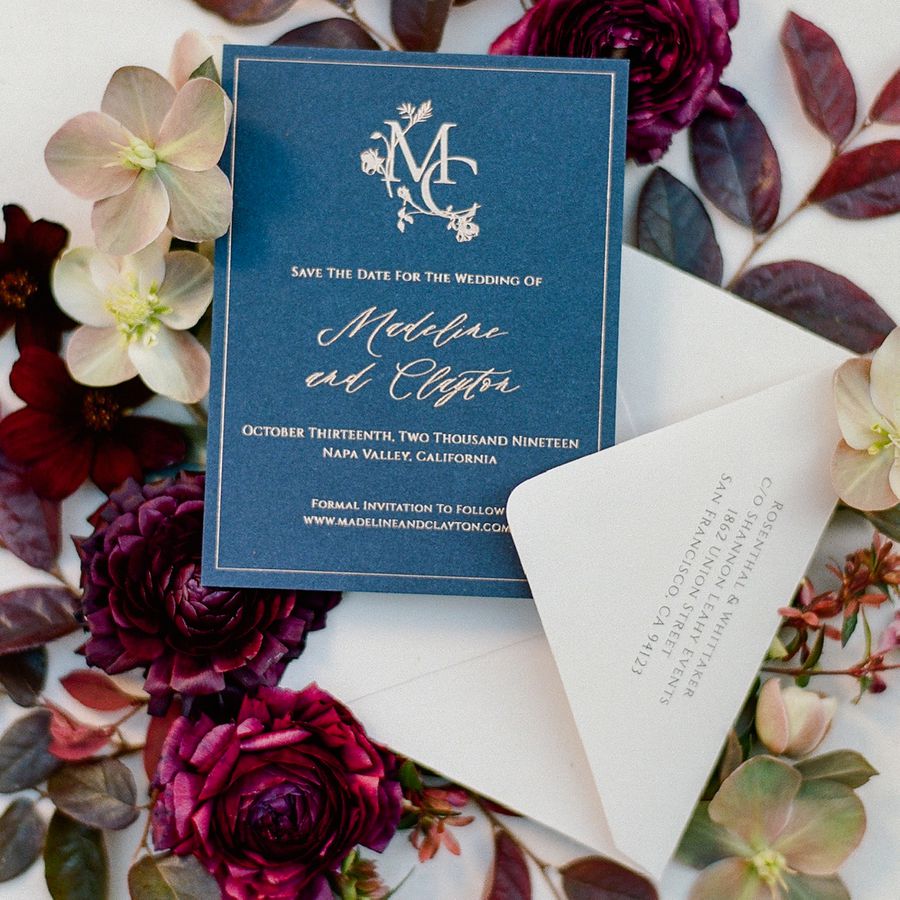save the date card with blue background and gold font on a bed of flowers