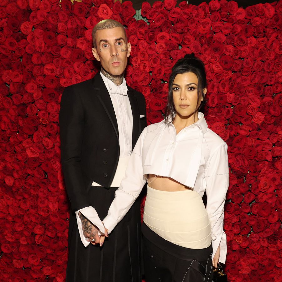 Travis Barker and Kourtney Kardashian posing in front of a wall of roses