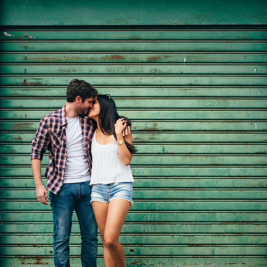 Couple standing and kissing with a green wall in the background 