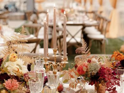 A fall-inspired tablescape with candelabras, golden ferns, and jewel-tone flowers