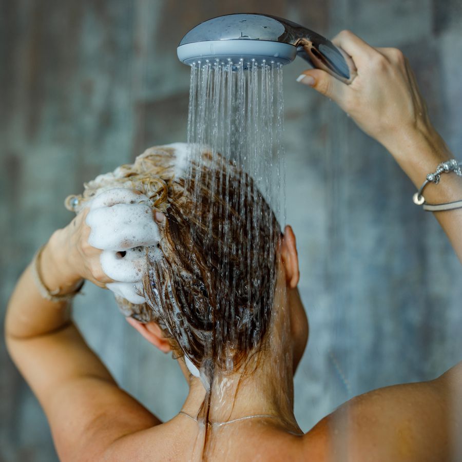 View of a woman washing her hair in the shower using thickening shampoo. 