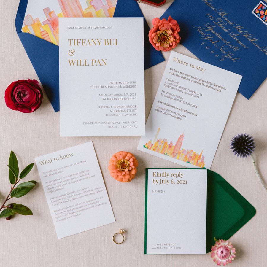 Opened wedding invitation laid out amongst flowers and a wedding ring