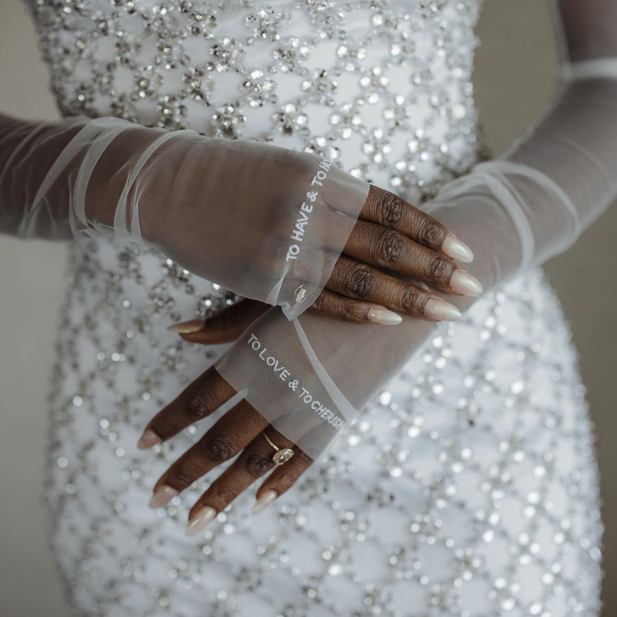 Bride's pearlescent nails and sheer gloves with an engraving rested on a sequined wedding dress