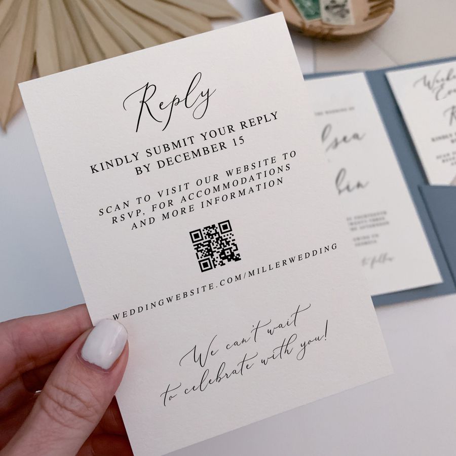 A woman with white nail polish holding a white wedding invitation with an RSVP QR code.