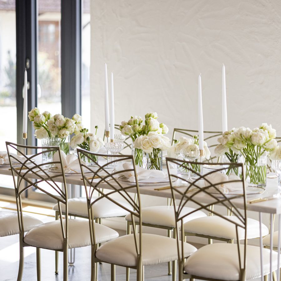 Rectangular table decorated with white taper candles and white flowers and gold chairs