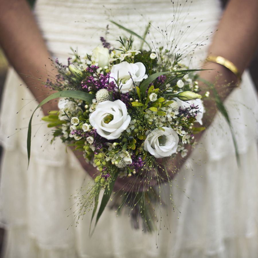 A bride in a white wedding gown holding a white, green, and purple floral bouquet.