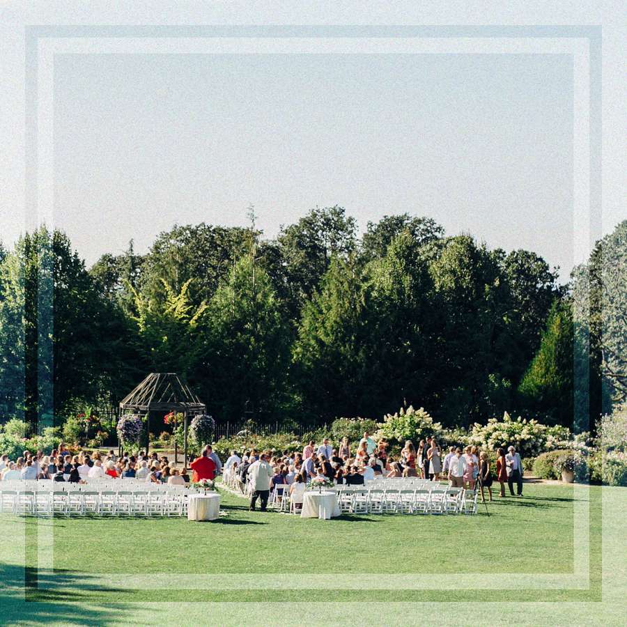 An outdoor wedding ceremony with guests seated in white chairs on a sweeping green lawn.