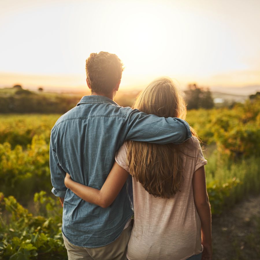 Young Couple With Arms Around Each Other Looking Over a Field at Sunset