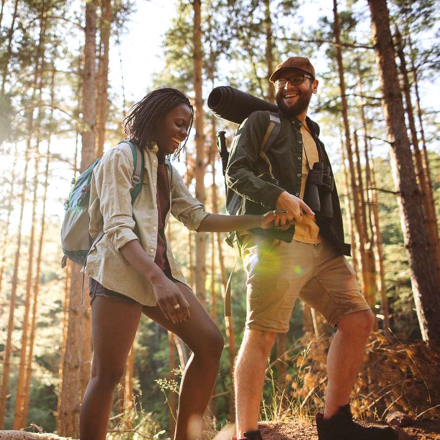 young happy couple holding hands as they hike through the forest at sunset