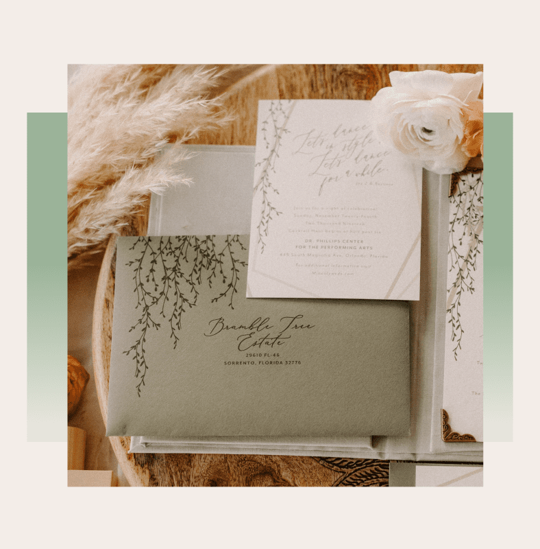 Flat lay of sage green invitation suite with bare wood and floral elements