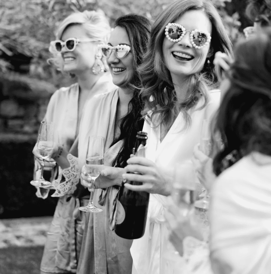 Bide and bridesmaids in sunglasses holding champagne and smiling